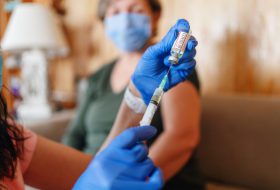 General practitioner vaccinating old patient at home with copy space. Doctor giving injection to senior woman at home. Nurse holding syringe and using cotton before make Covid-19 or coronavirus vaccine.