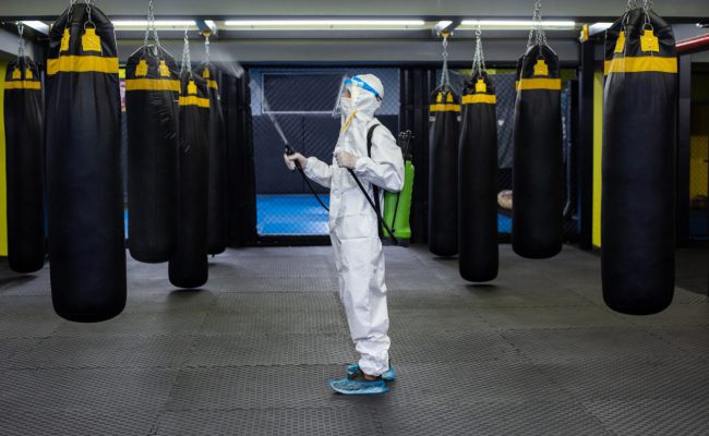 A mid adult woman in protective gear disinfecting a gym.